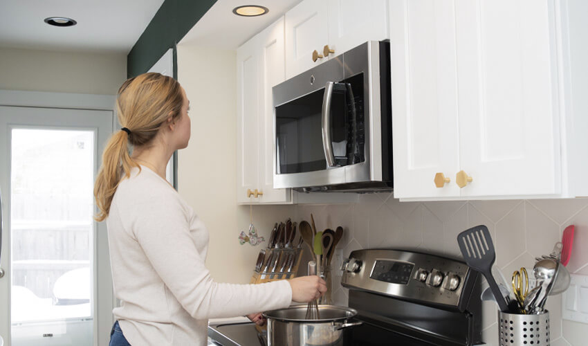 Woman looking up at overhead pot light while stirring something on stovetop