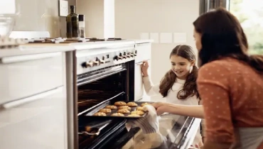 A parent and child putting cookies into the oven of a drop-in range | freestanding-vs-slide-in-range-hero.