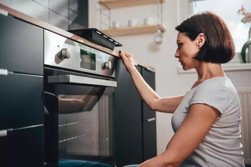 Woman crouched down in kitchen looking at a self-cleaning oven.