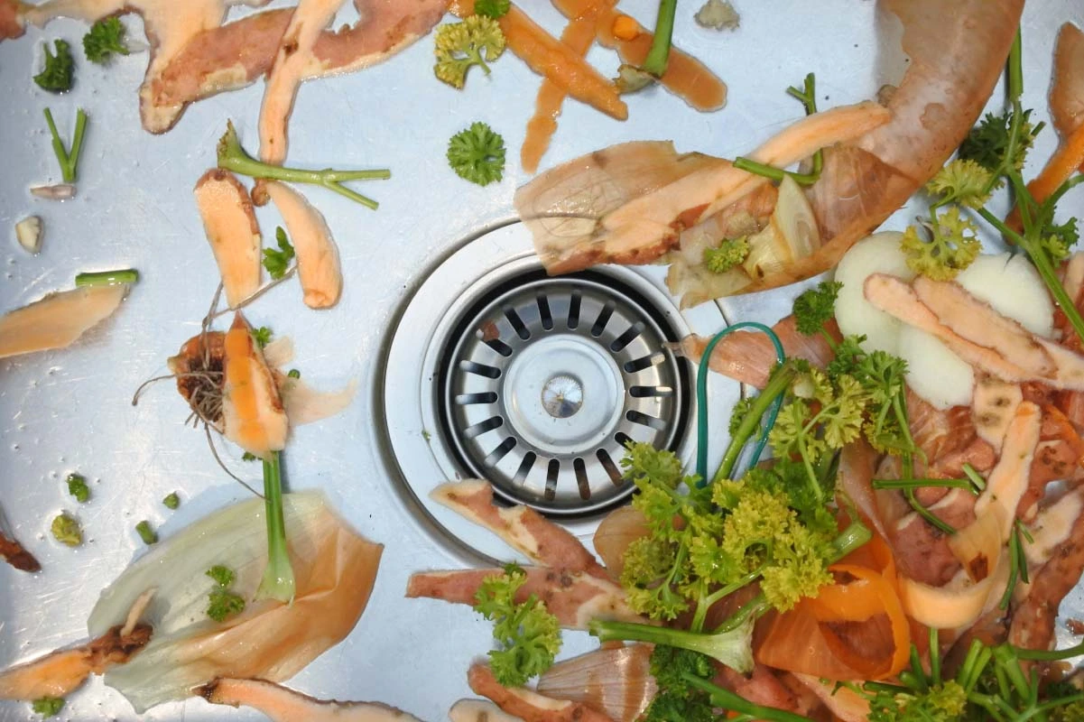 Sink filled with food scraps near garbage disposal.