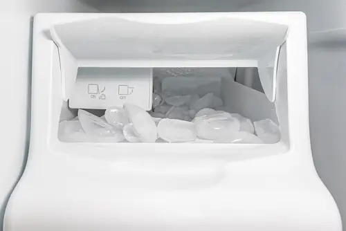 Freezer ice maker close to overflowing with ice.