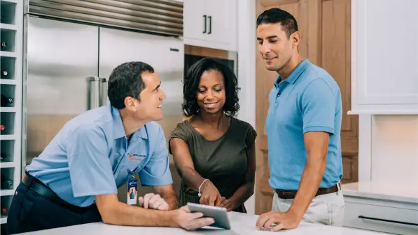 A Mr. Appliance service professional explaining kitchen appliance repairs to homeowners.