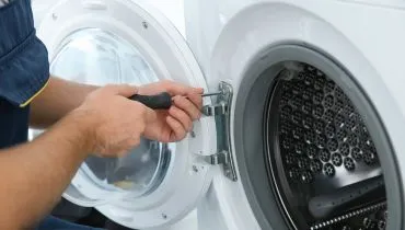 A service professional using a screwdriver to repair the dryer door.