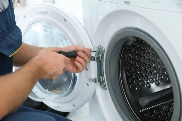 A service professional using a screwdriver to repair the dryer door.