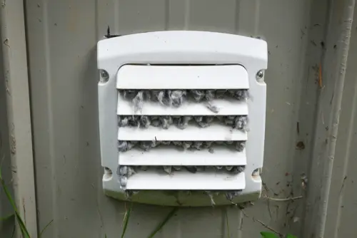 A dirty exterior dryer vent flap clogged with lint.