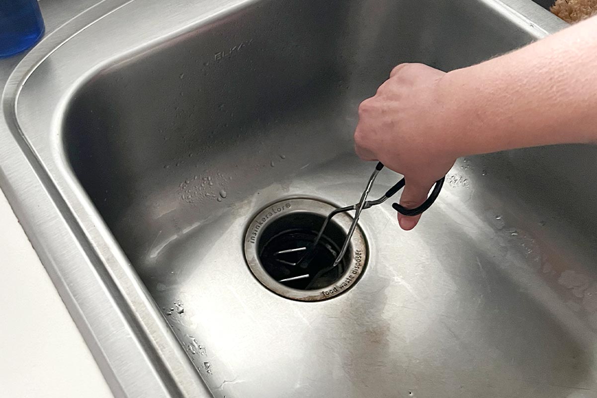 Use tongs or needle-nose pliers to remove any visible food or debris from a clogged garbage disposal.
