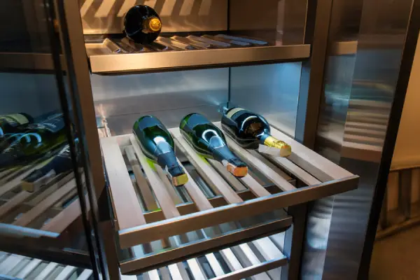 Wine bottles on wooden racks inside a freestanding wine cooler.