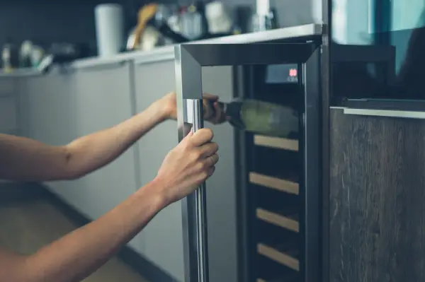 Woman grabbing a wine bottle from a built-in wine cooler installed beneath a counter.